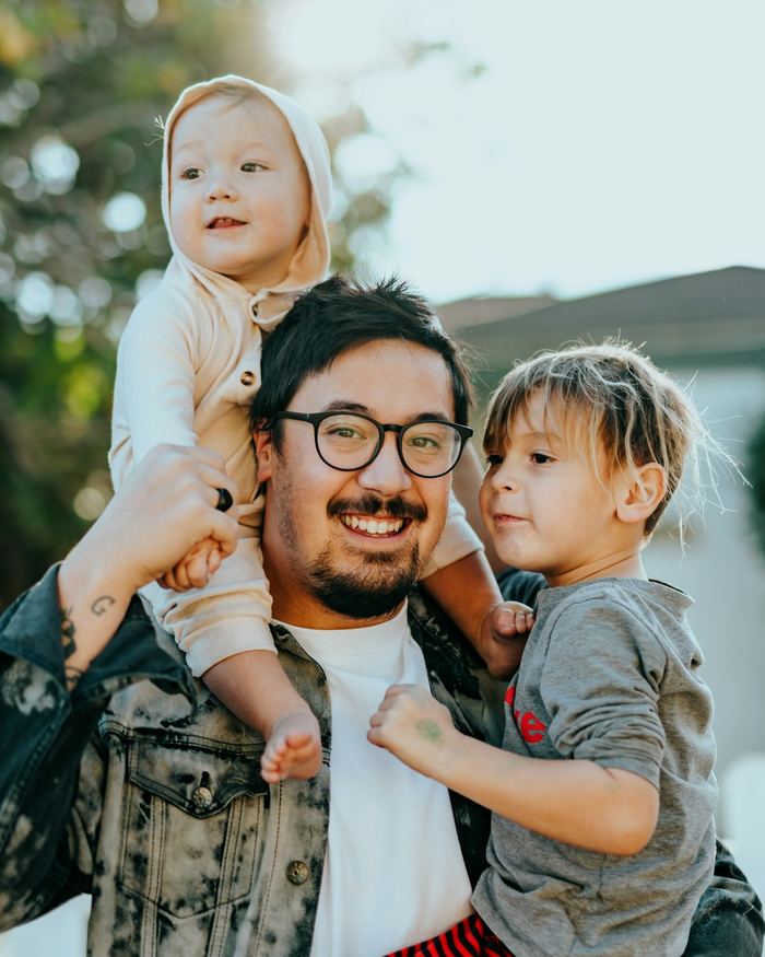 A smiling dad carrying his two young kids outside their home